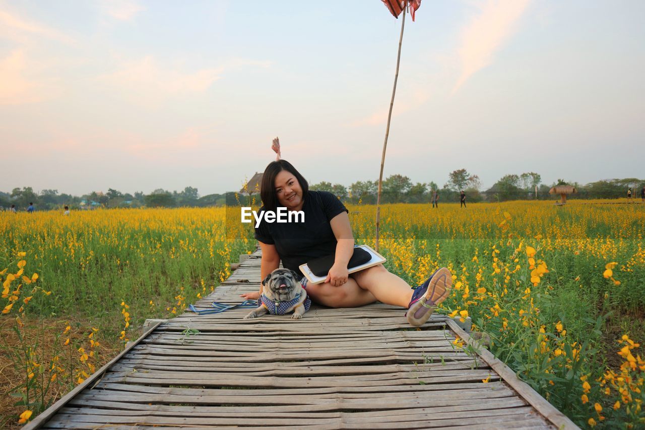 Full length portrait of young woman sitting on land against sky