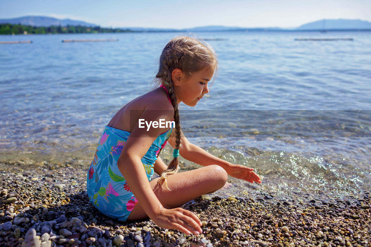 Girl has fun and plays with stones on pebble beach at geneva lake, summer vacations and travel