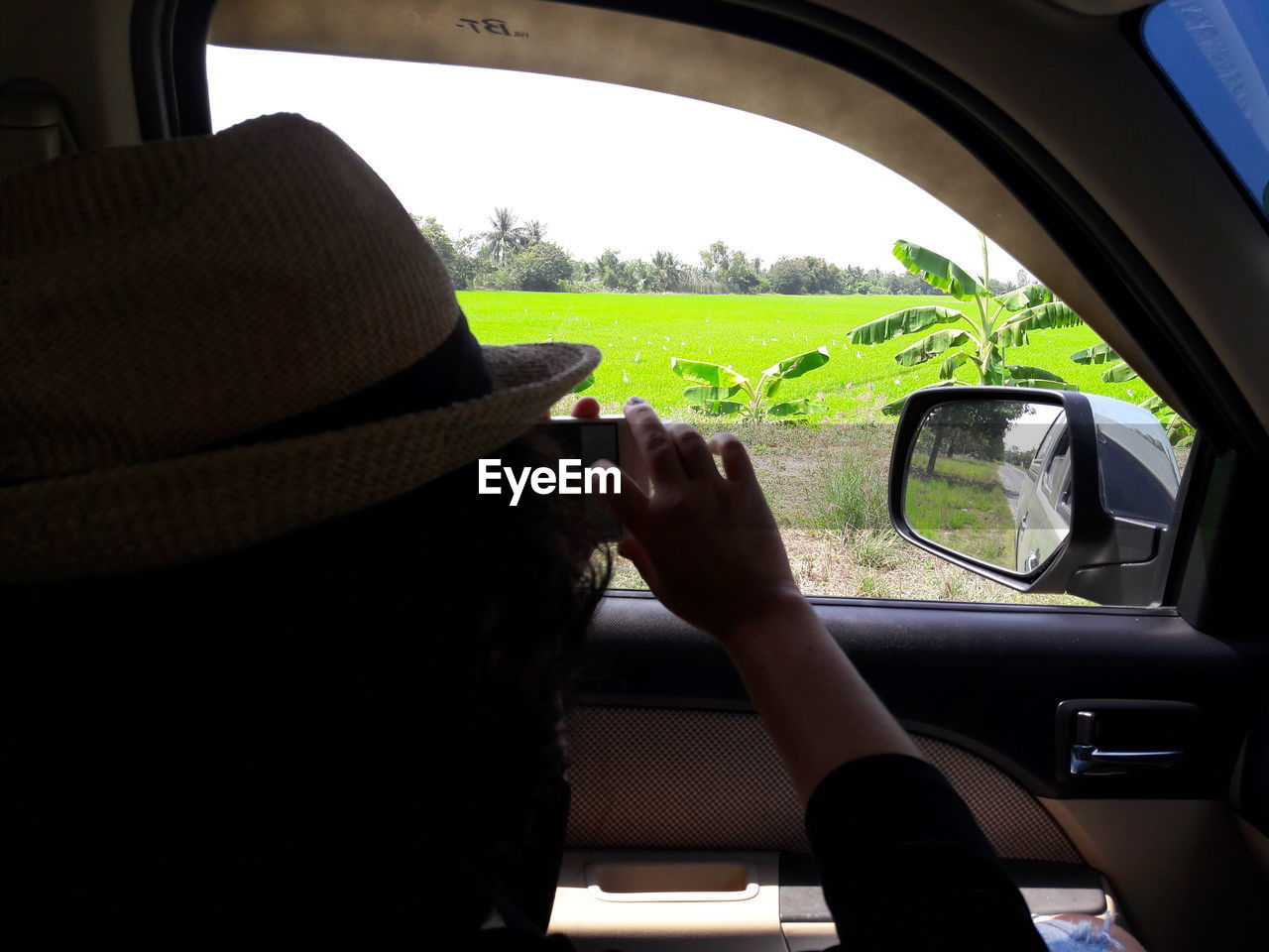Woman photographing field while traveling in car