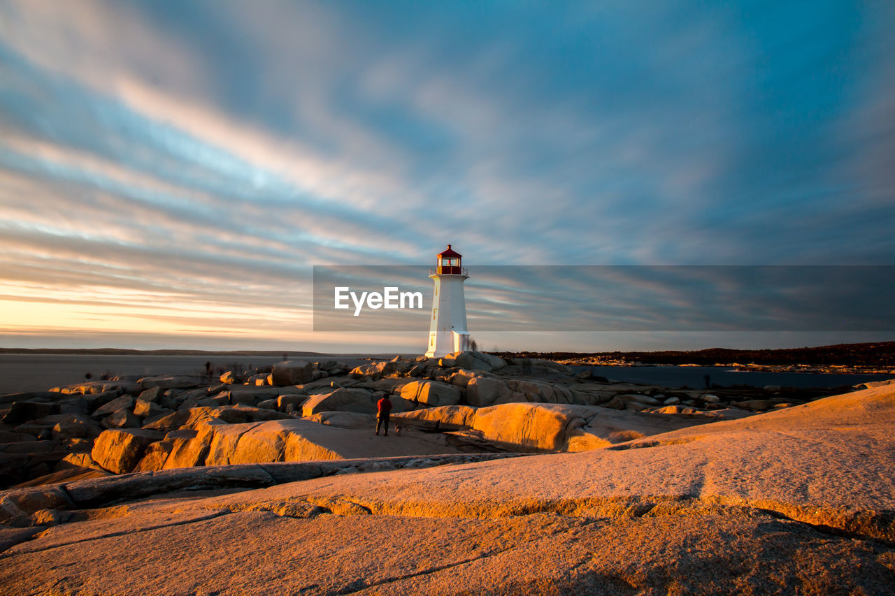 Lighthouse on rock against cloudy sky during sunset