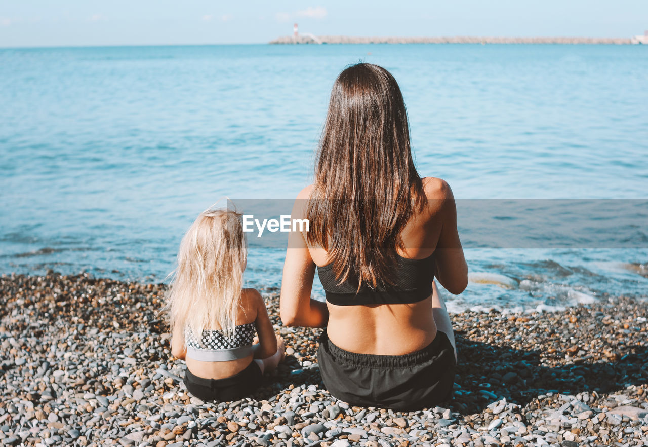 Rear view of mother and daughter sitting at beach