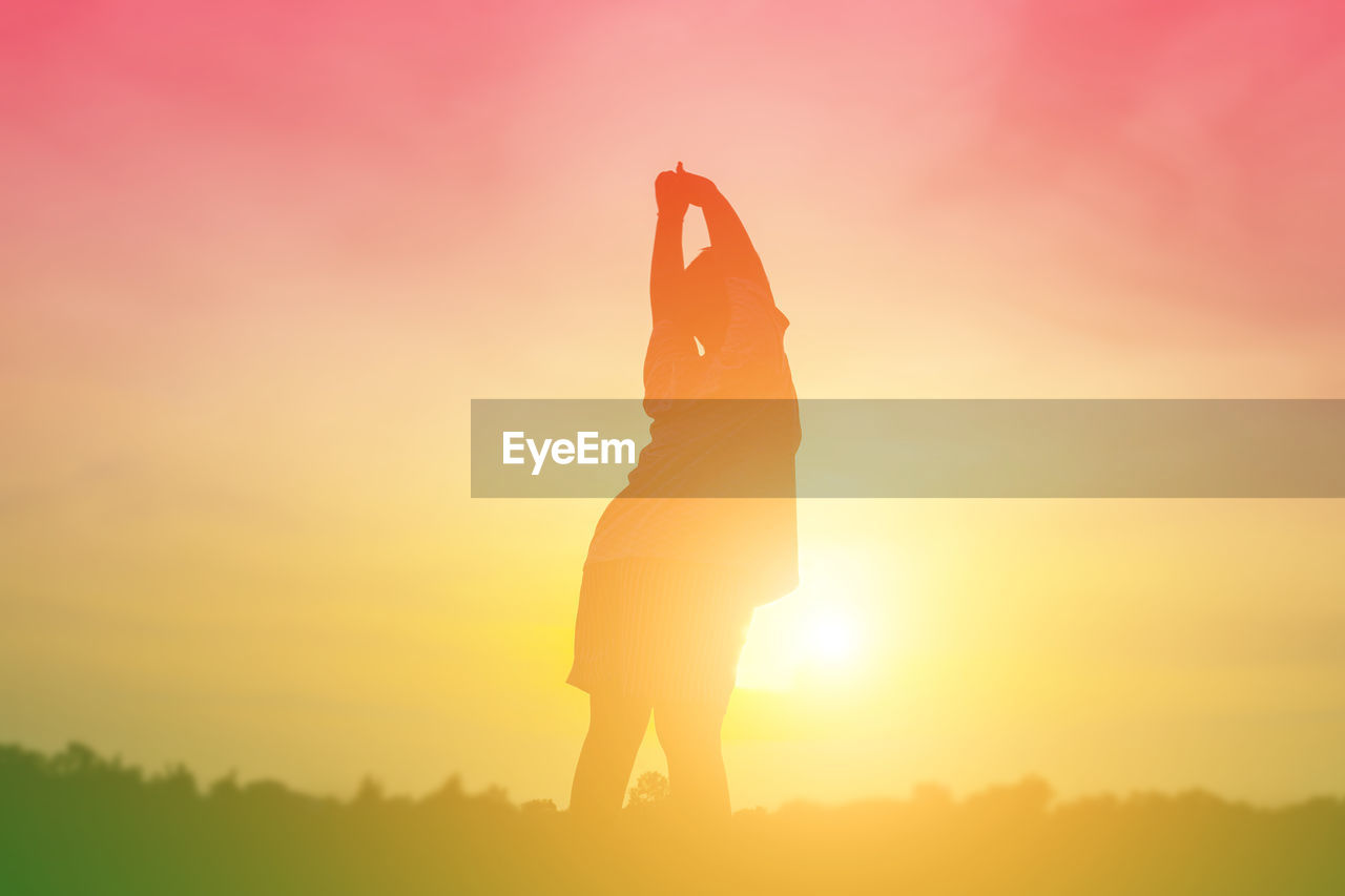 Silhouette man with arms raised standing against orange sky