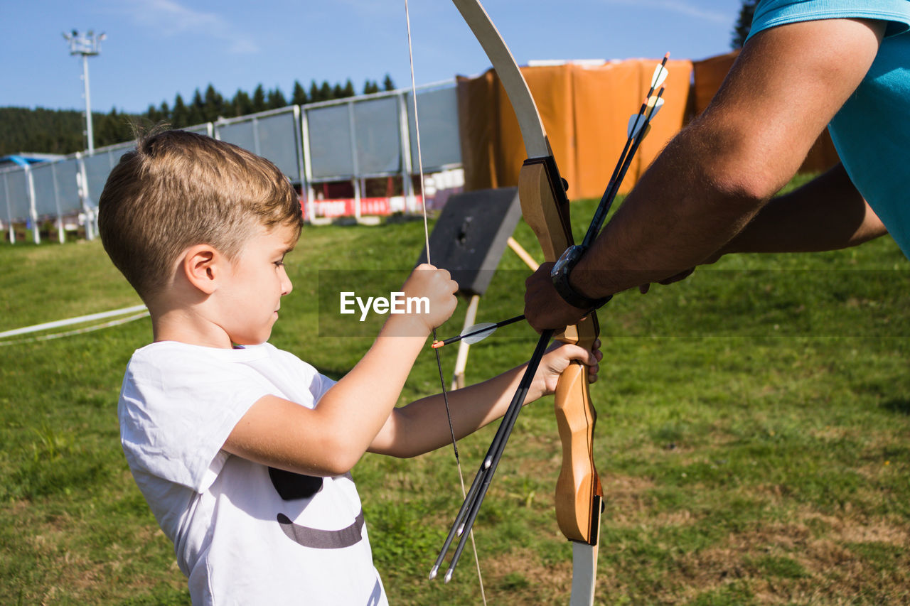 Coach giving archery training to boy outdoor