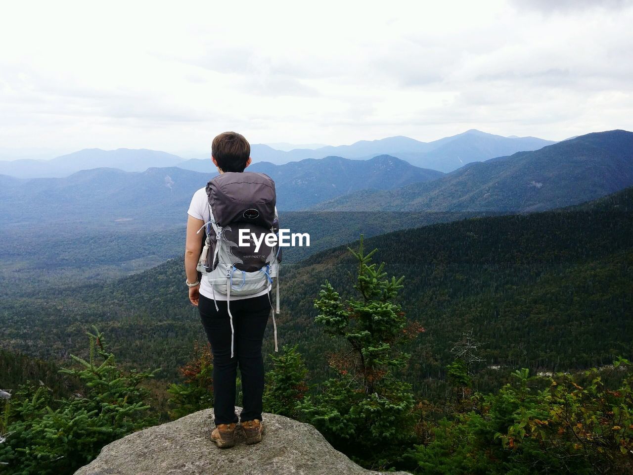 Rear view of hiker standing on cliff in front of mountains