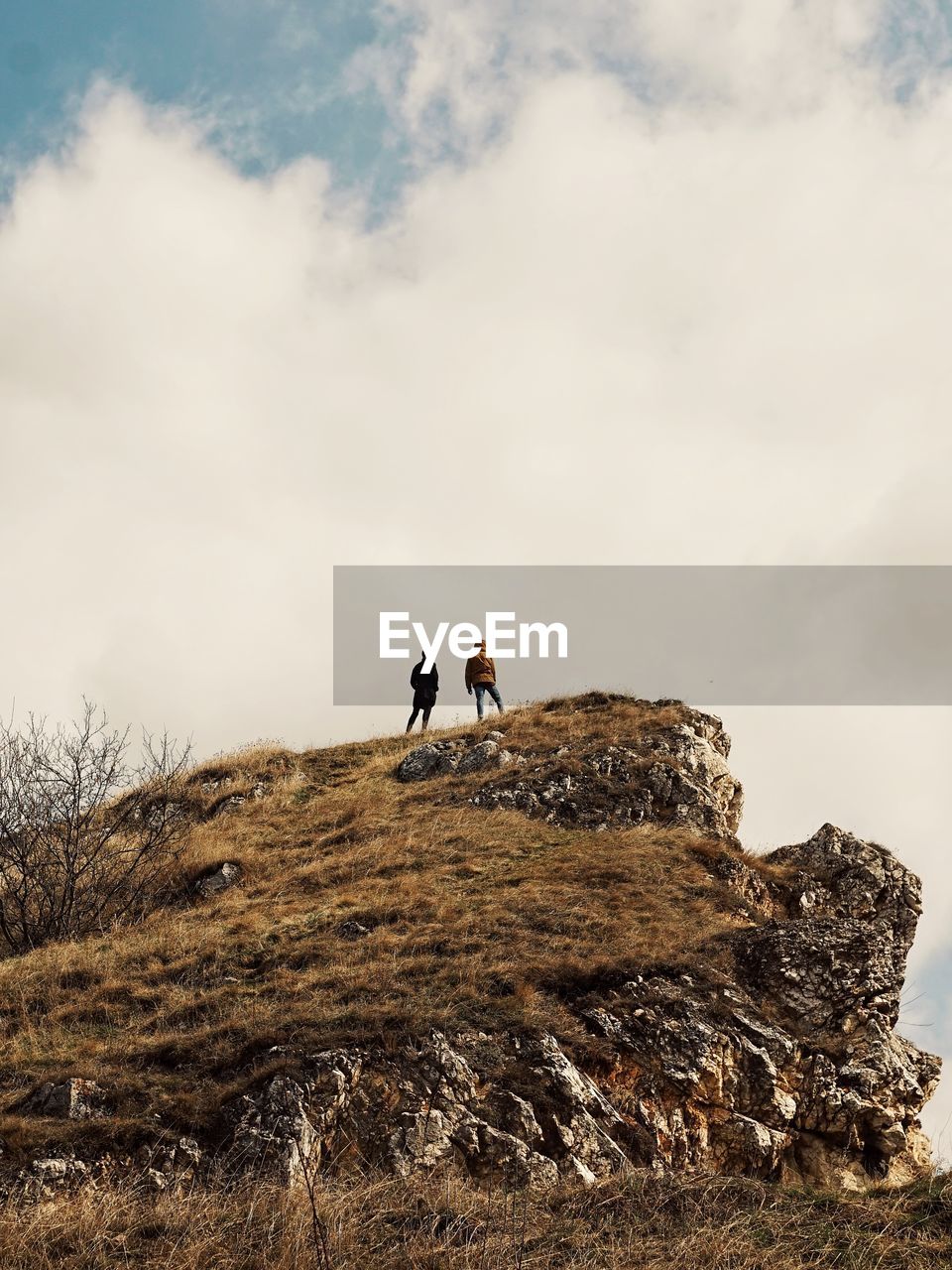 Low angle view of people standing on rock against cloudy sky