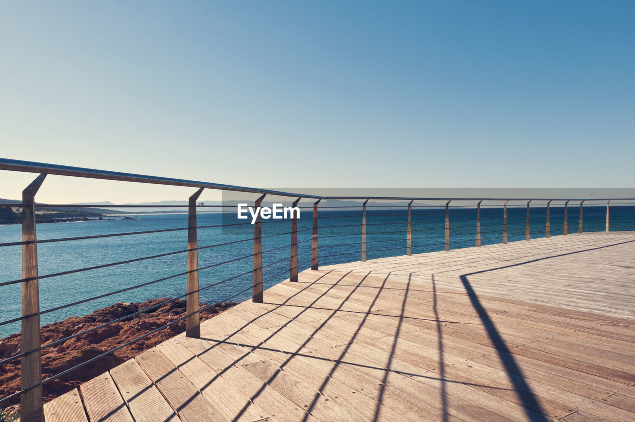 Railing by sea against clear sky