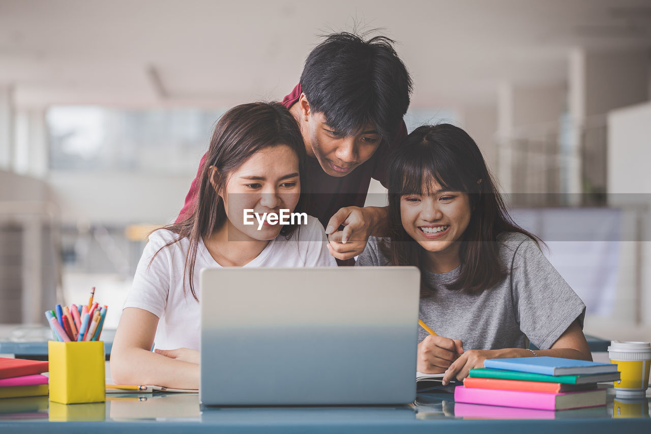 Happy friends using laptop on table