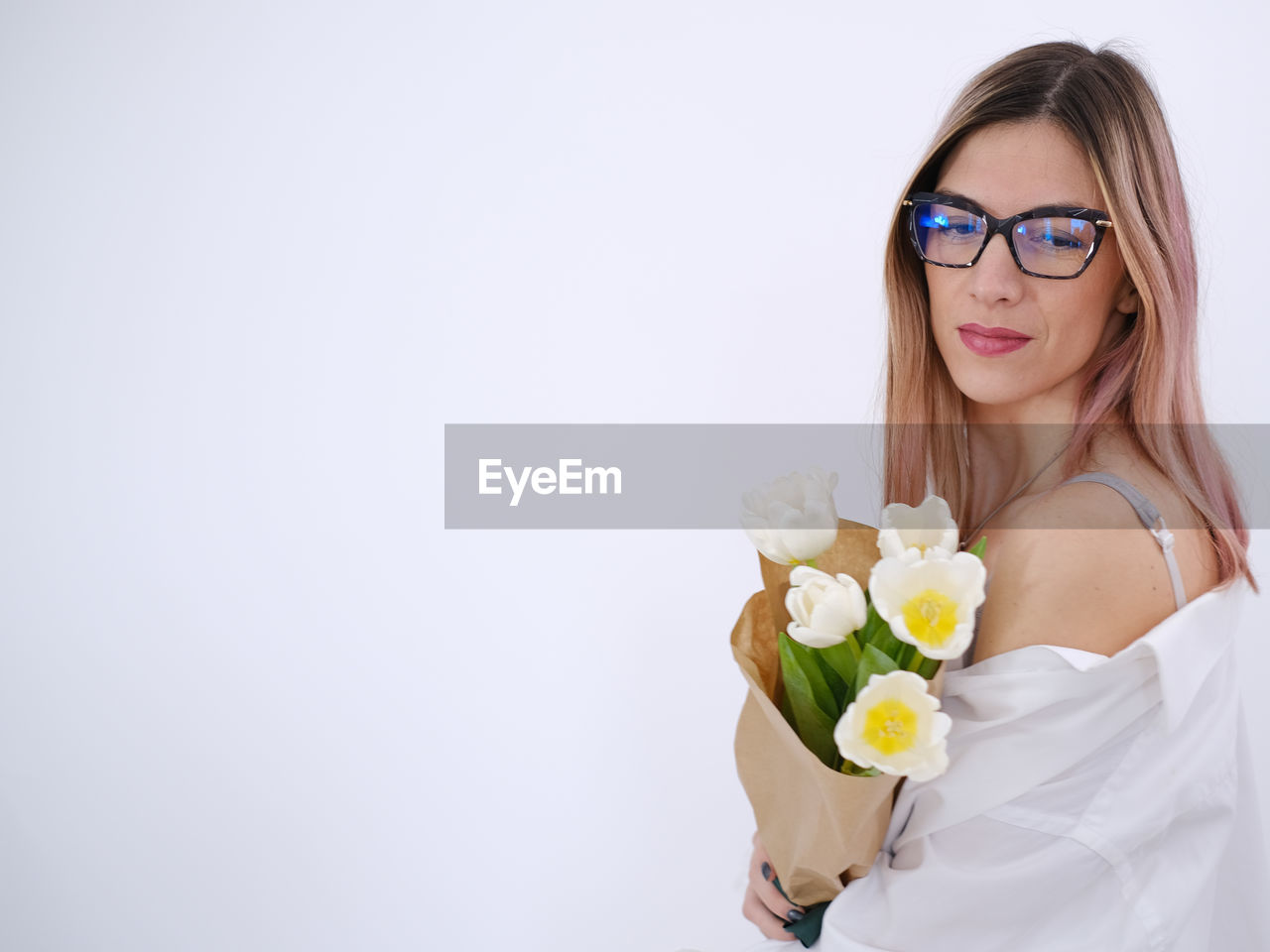 Woman in white shirt holding a bouquet of white tulips on a white background.