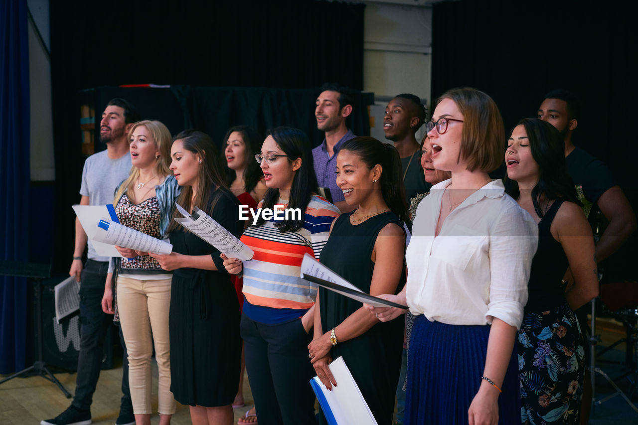 Multi-ethnic male and female students singing in choir at auditorium
