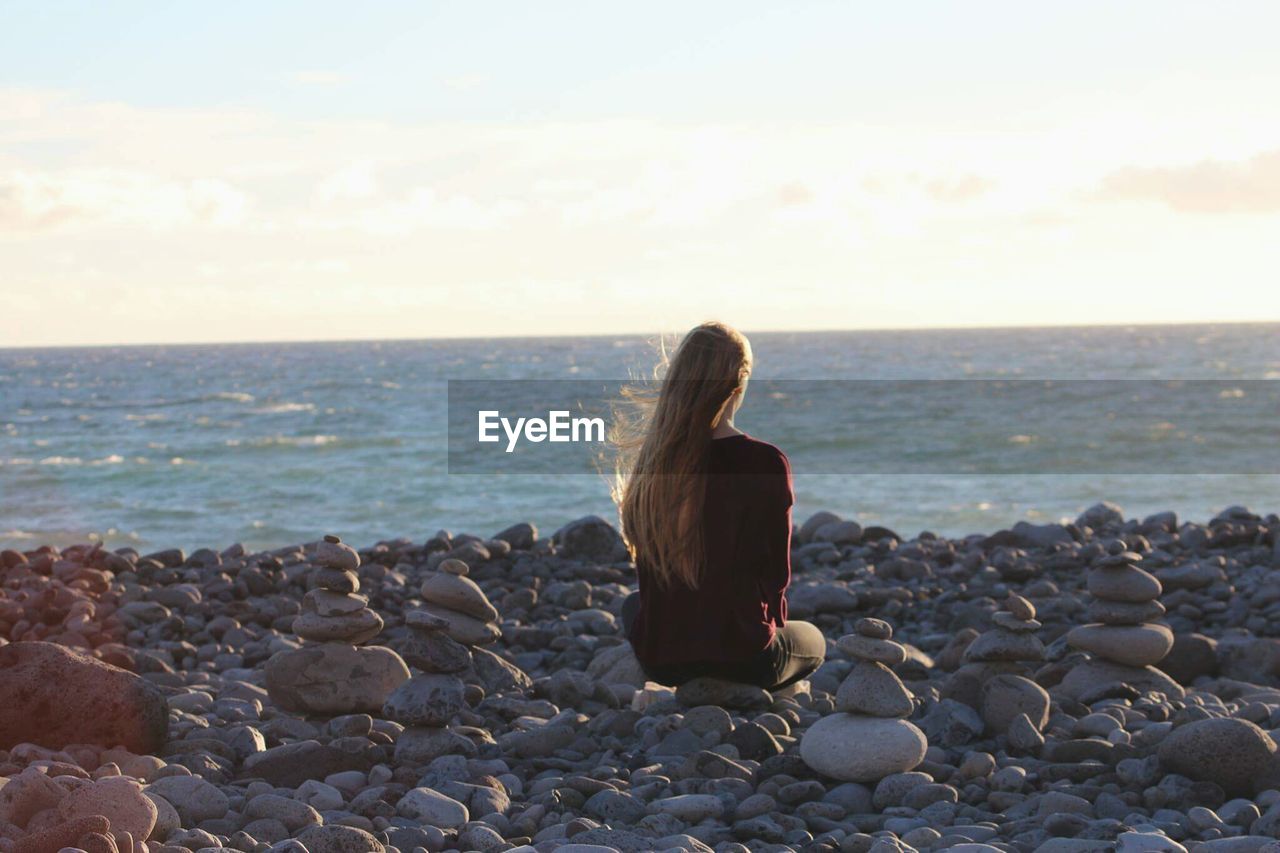 Woman sitting on rocks at beach against sky