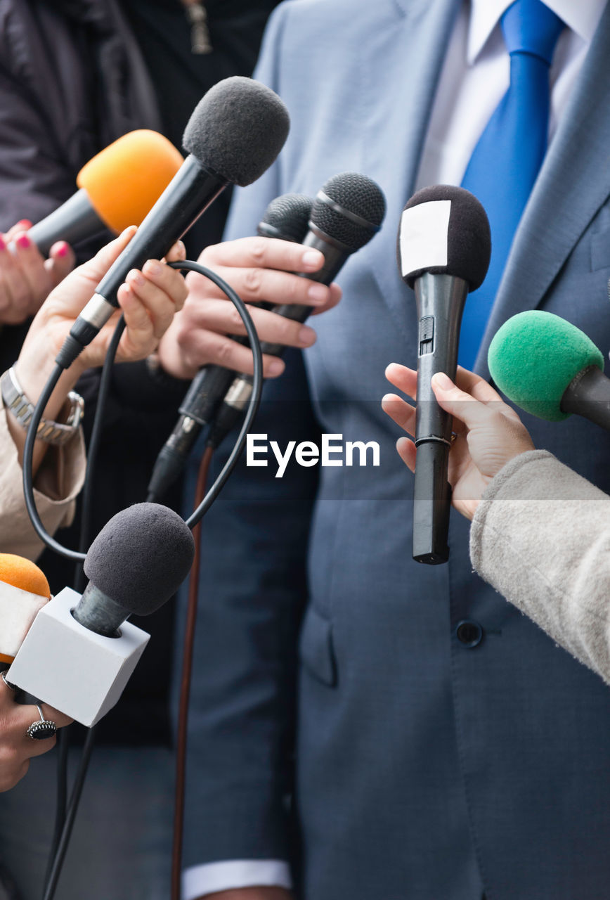 Cropped hands of journalists holding microphones in front of businessman