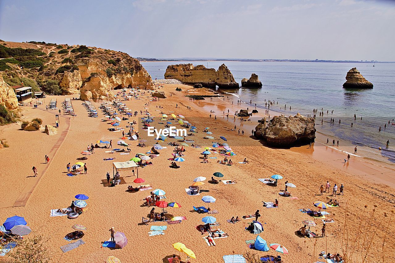 HIGH ANGLE VIEW OF CROWD ON BEACH AGAINST SKY