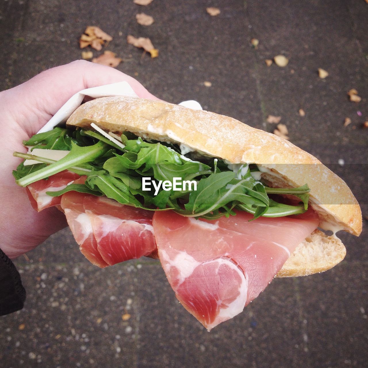 Cropped image of hand holding sandwich at street