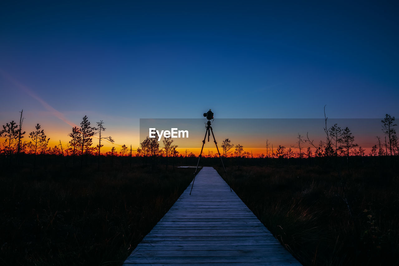 BOARDWALK ON FIELD AGAINST CLEAR BLUE SKY DURING SUNSET