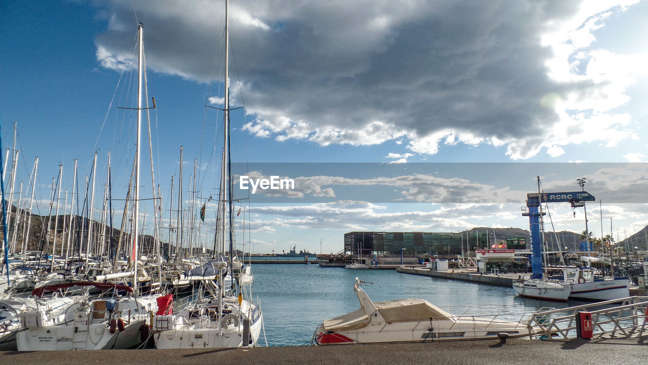 Sailboats moored at harbor against sky