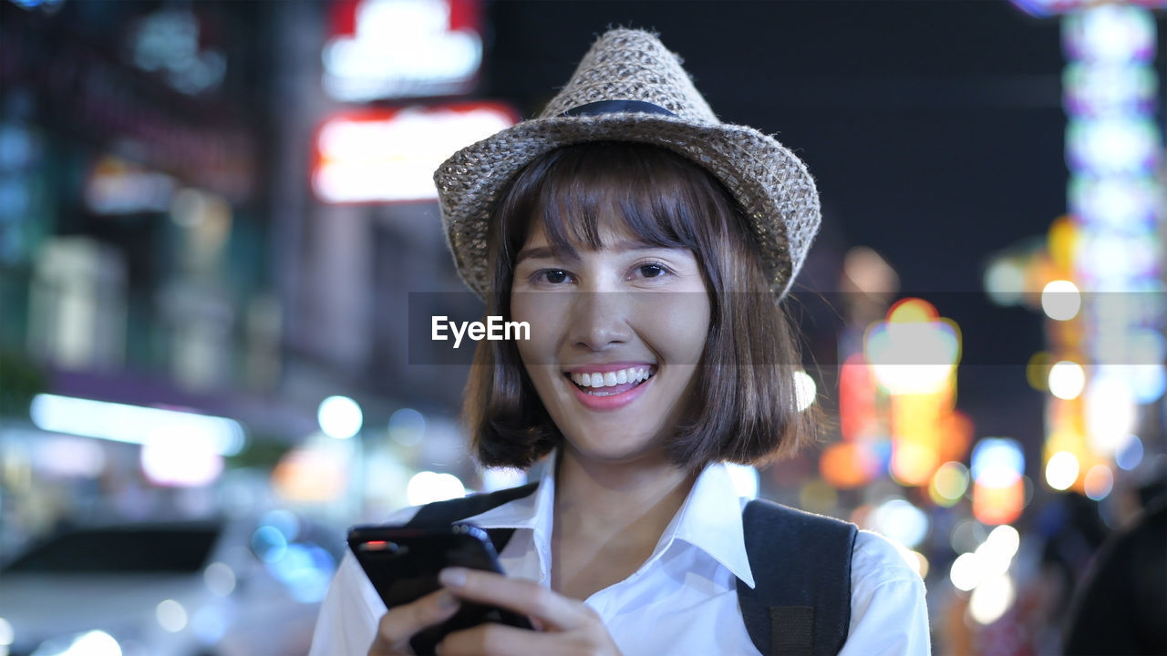 Portrait of smiling woman using mobile phone in city at night