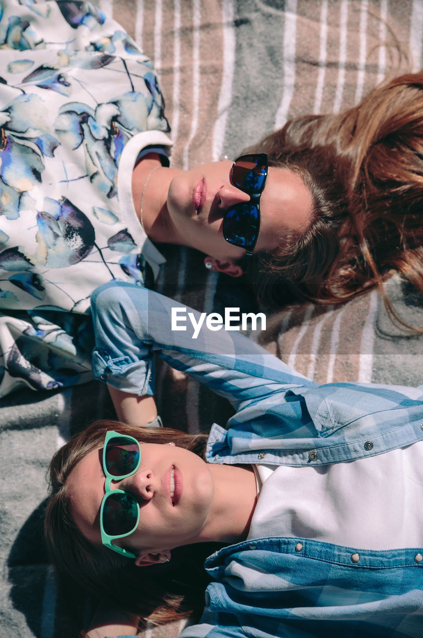 High angle view of friends wearing sunglasses while lying on blanket in forest