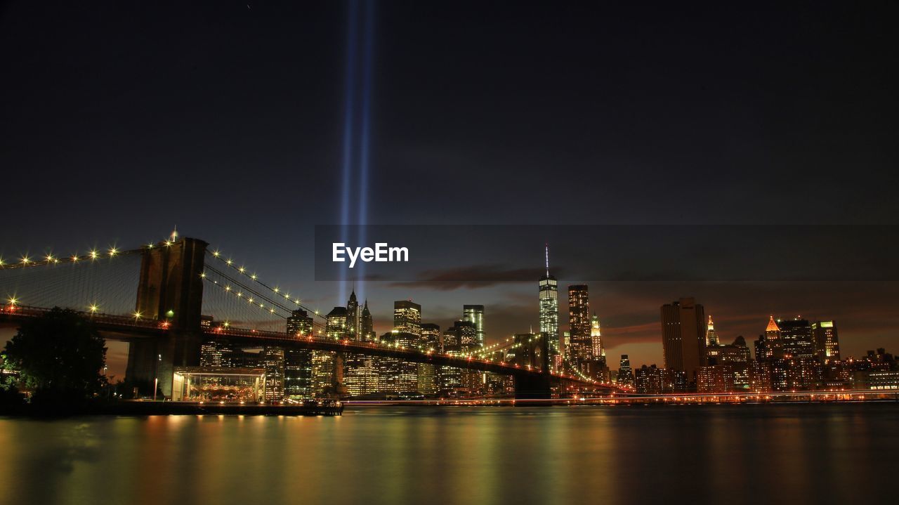 Brooklyn bridge over east river against sky in illuminated city at night