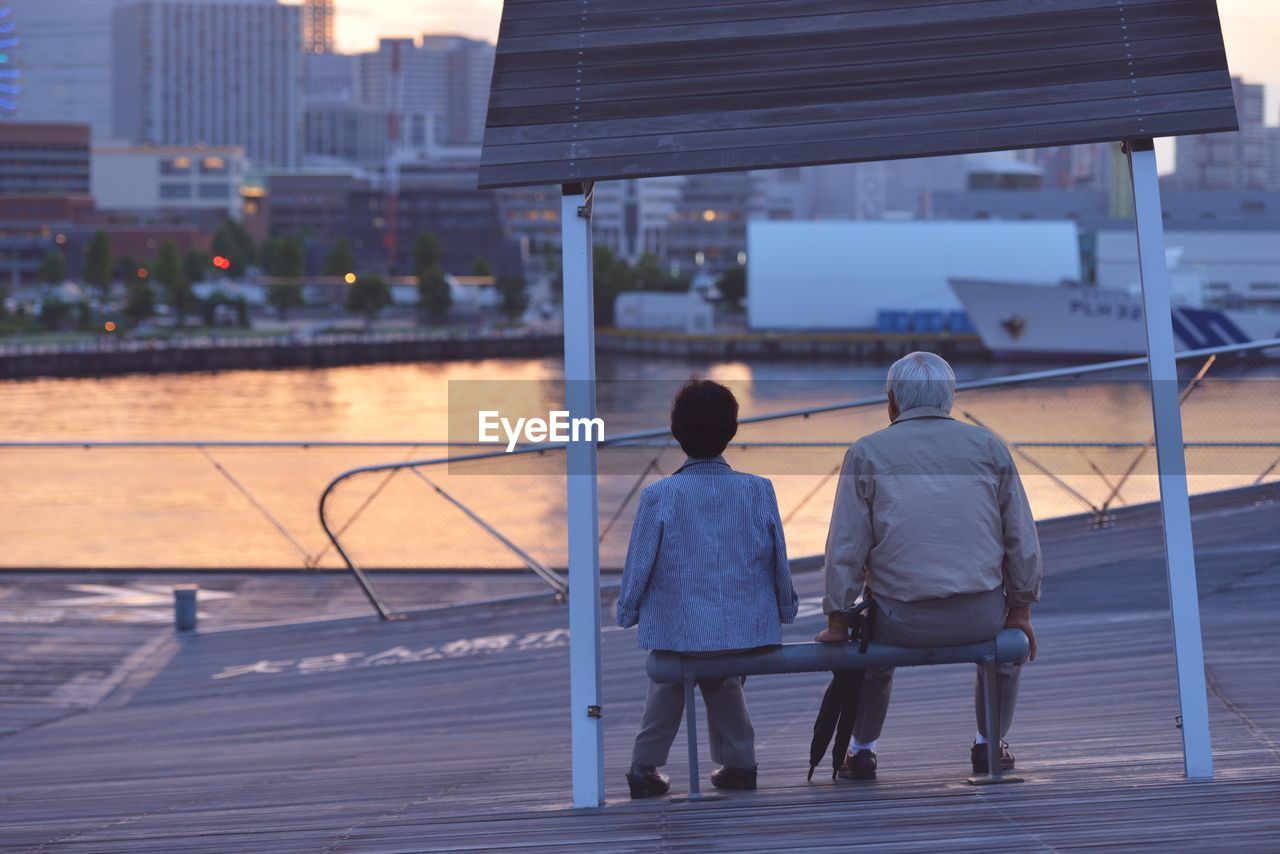 Rear view of two people sitting on bench