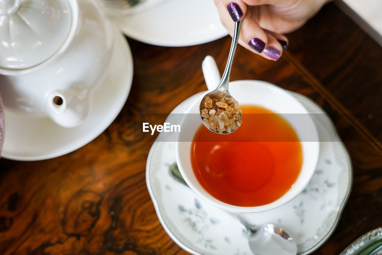 Cropped hand putting brown sugar in tea