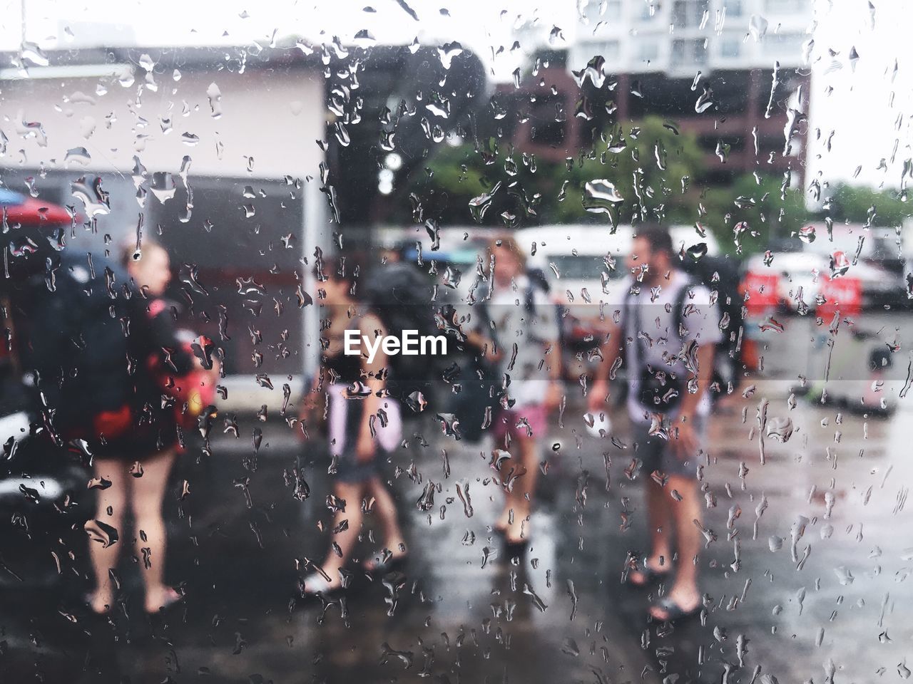 PEOPLE SEEN THROUGH WET GLASS WINDOW