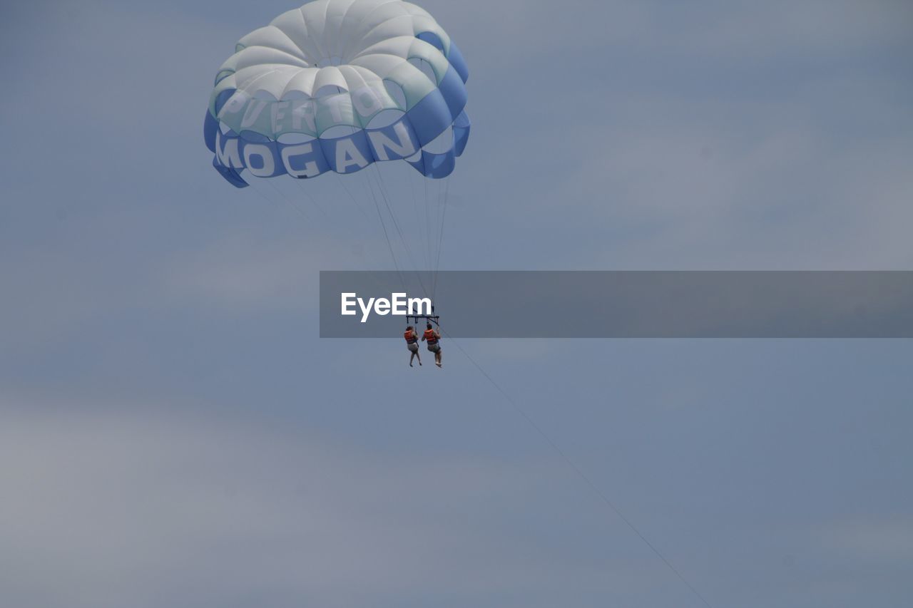 Low angle view of people paragliding against sky