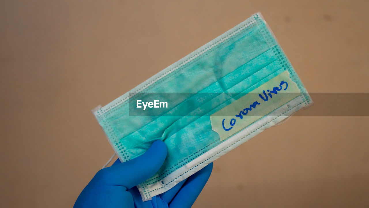 Close-up of hand holding mask with coronavirus text against wall