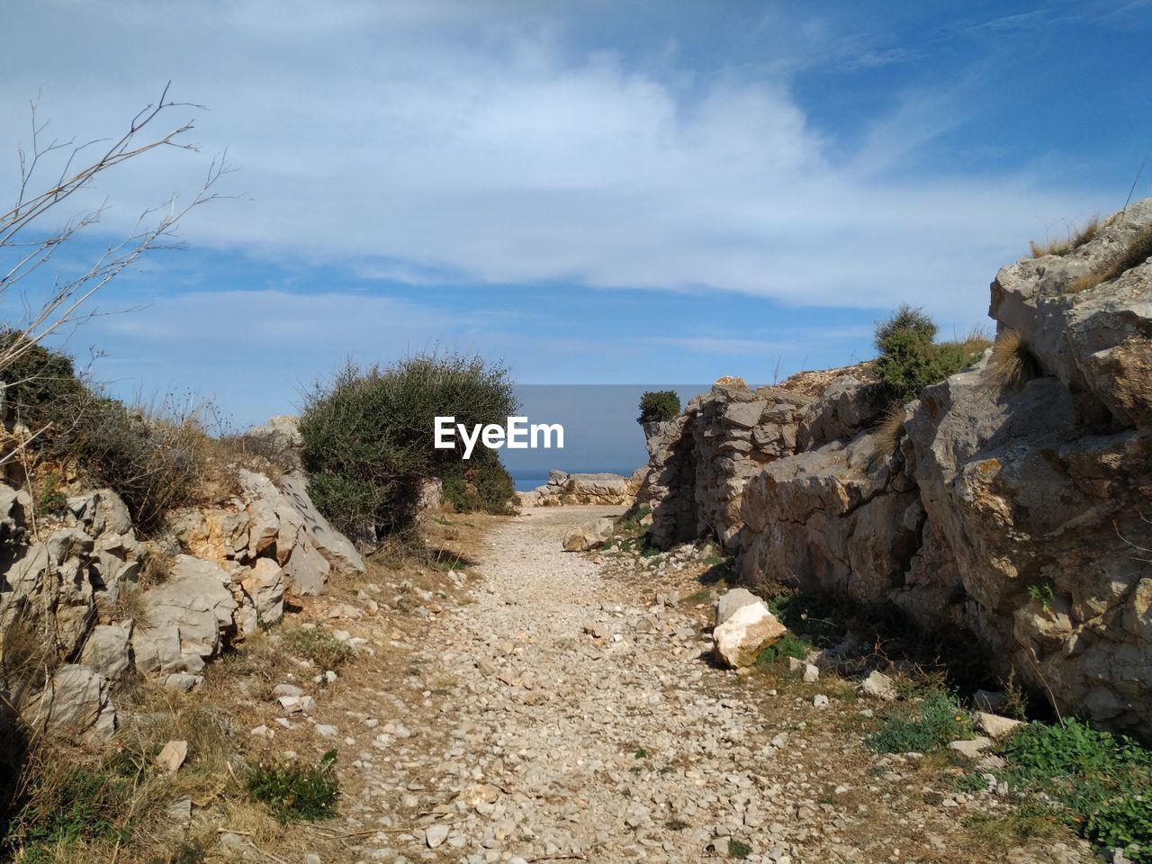 Dirt road amidst rocks against sky