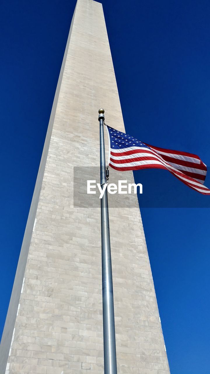Low angle view of american flag by obelisk against clear blue sky