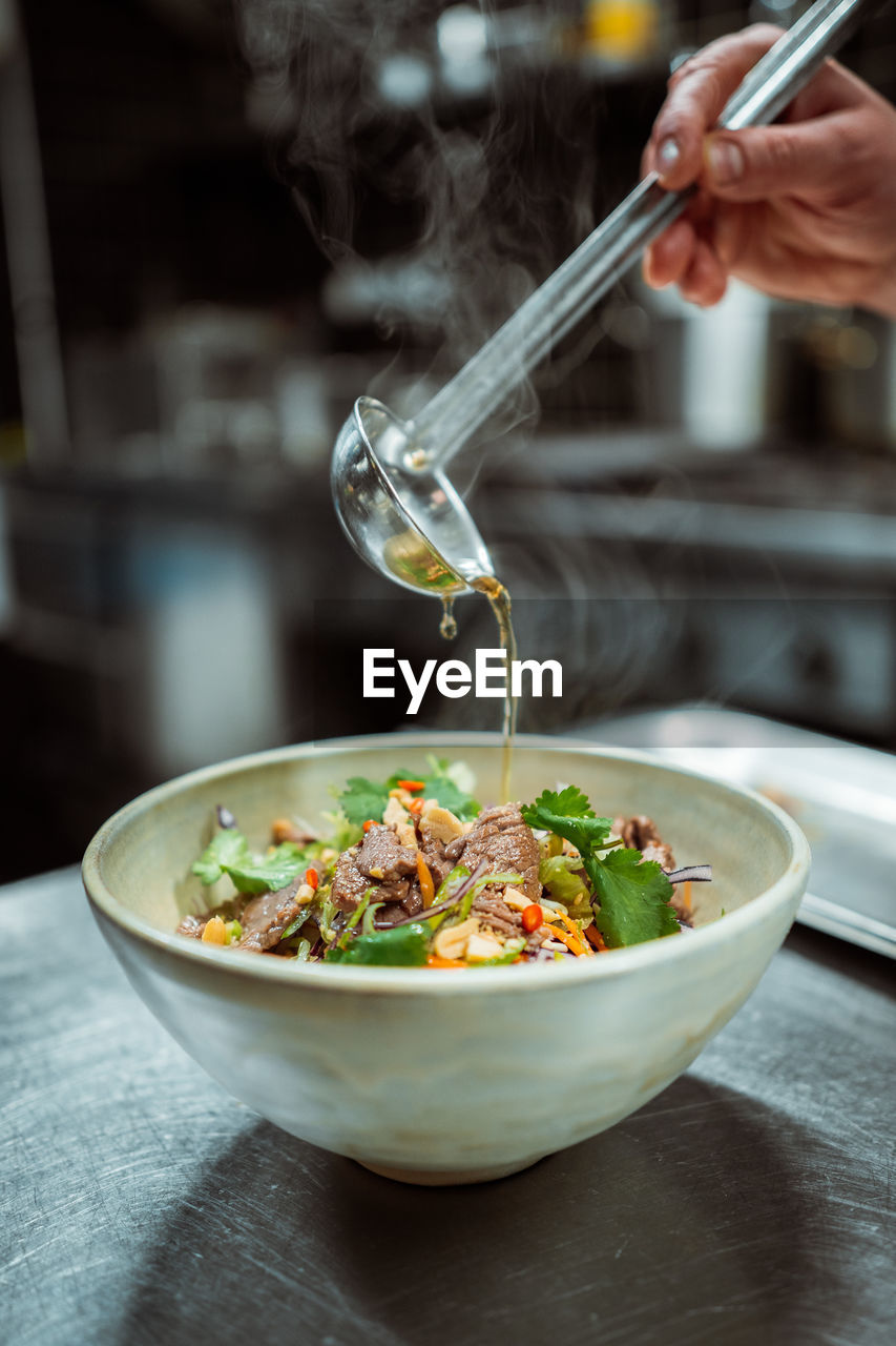 Vertical view of the unknown man hand pouring oil or sauce from ladle to the bowl with meat