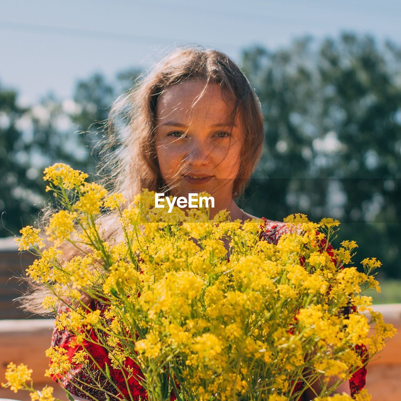 Portrait of young woman with yellow flowers against blurred background
