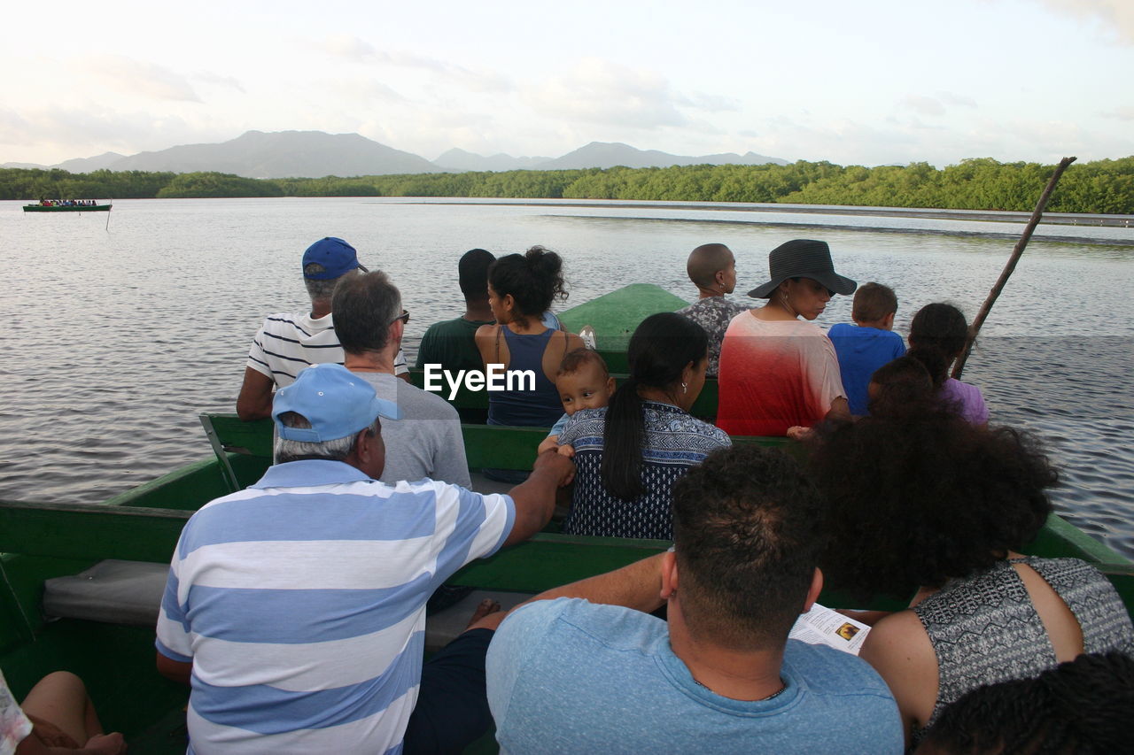 REAR VIEW OF PEOPLE SITTING ON LAKE