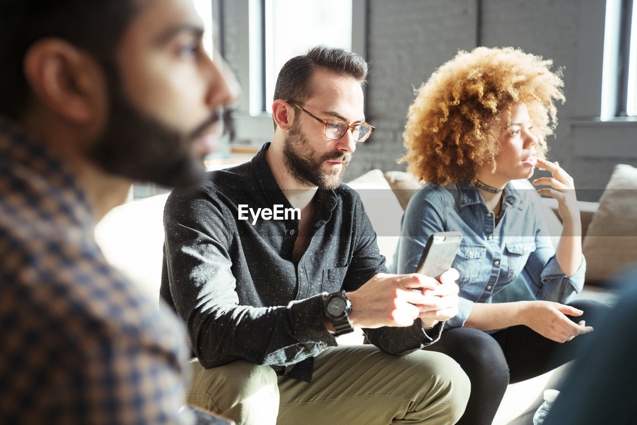 Businessman using mobile phone while sitting with colleagues in office