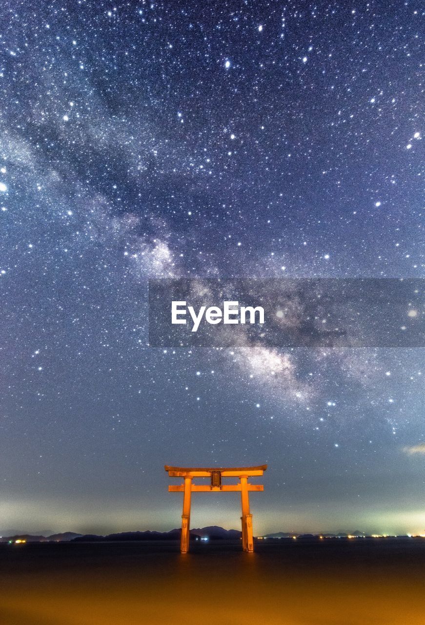 Low angle view of stars over torii gate and river against sky at night