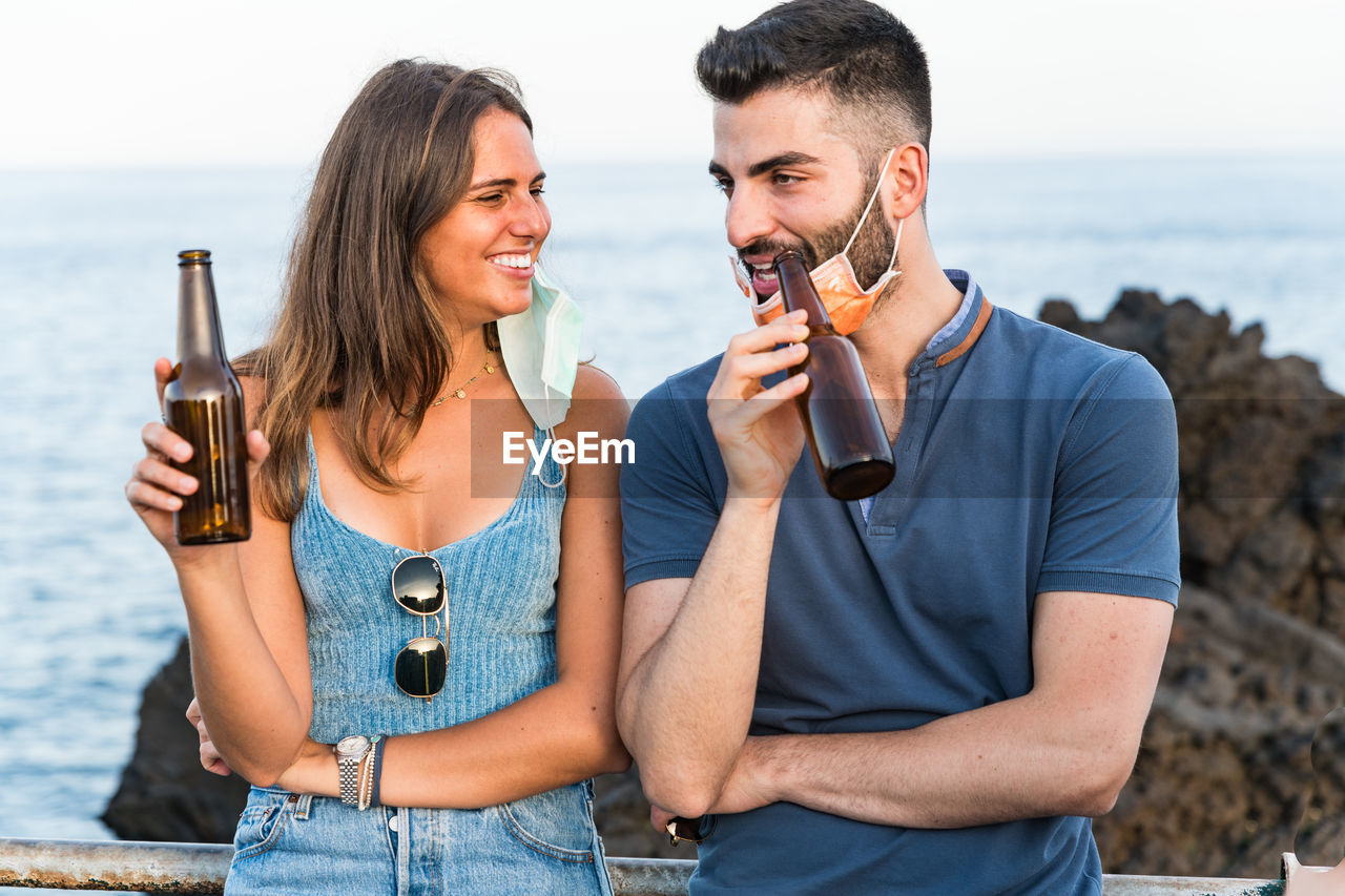 Smiling couple having drink while standing at beach