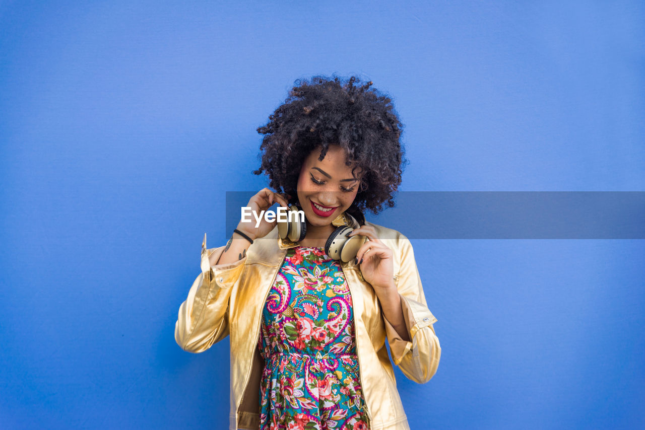 Fashionable young woman with curly hair against blue background