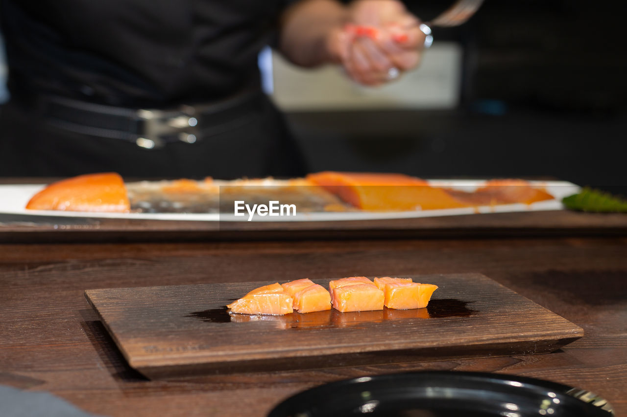 Chef slicing salmon on black wooden table in a restaurant.