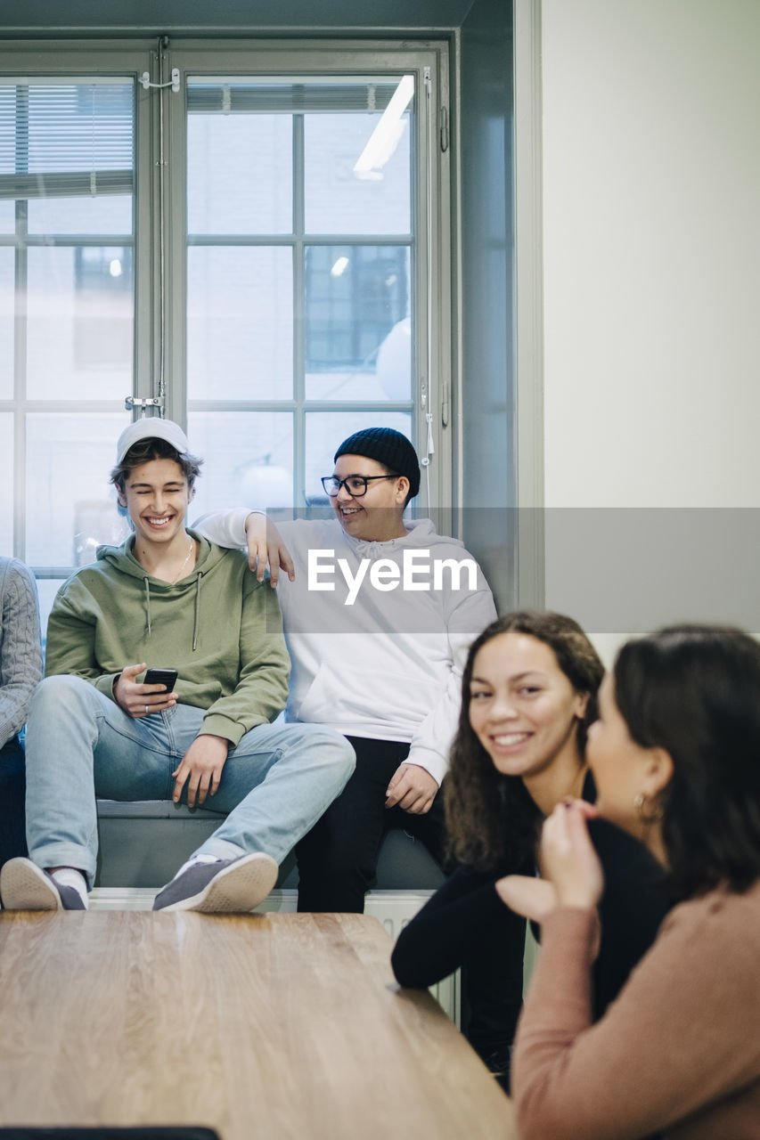 Smiling teenage students talking while sitting classroom