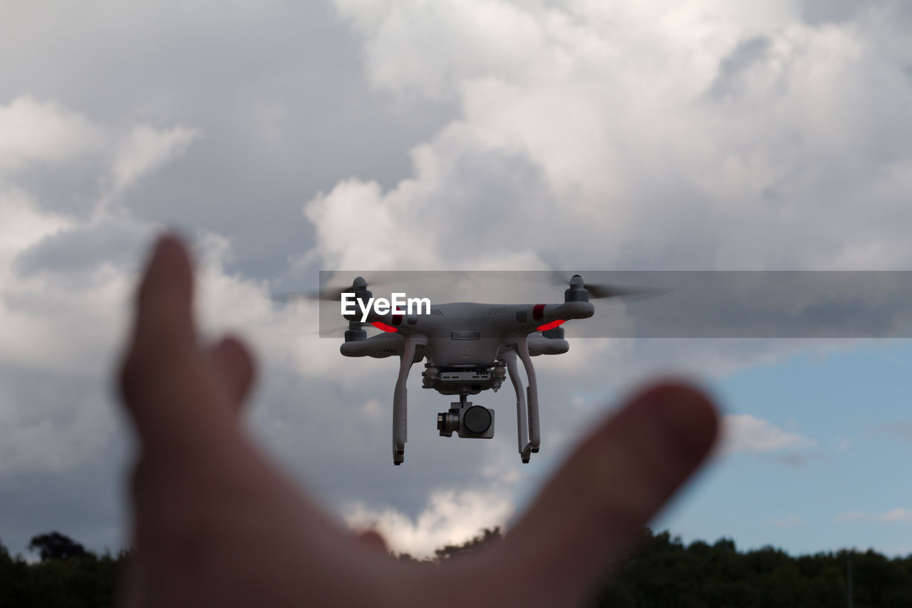 Cropped hand of person reaching drone against sky