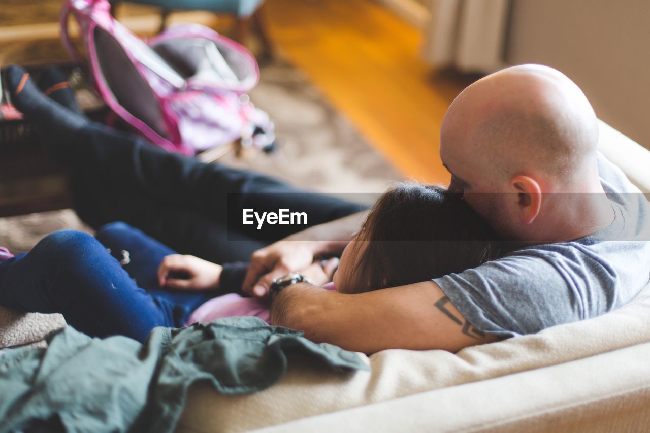 High angle view of father sitting with daughter on sofa