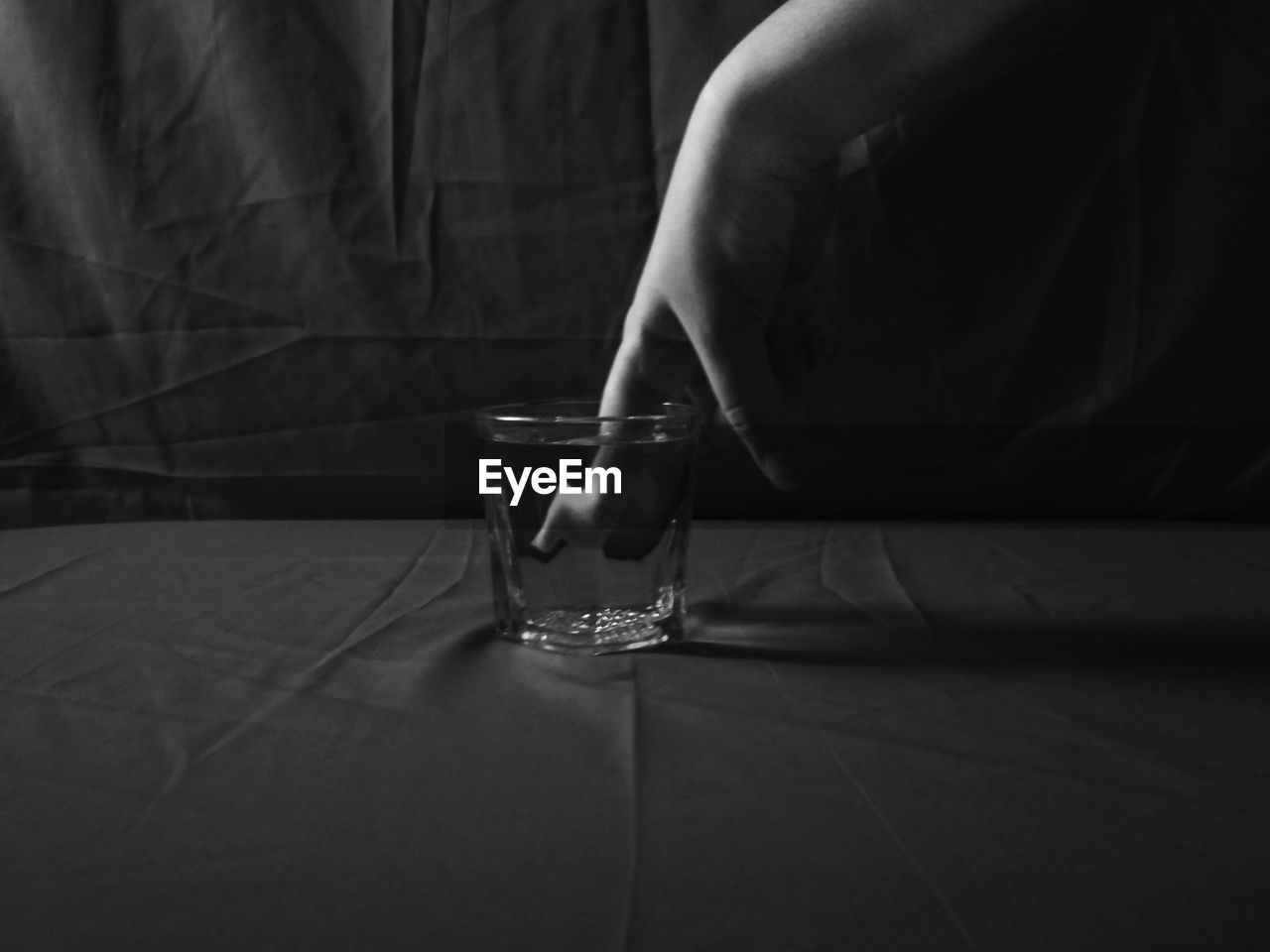 Close-up of woman hand in glass of water against black background