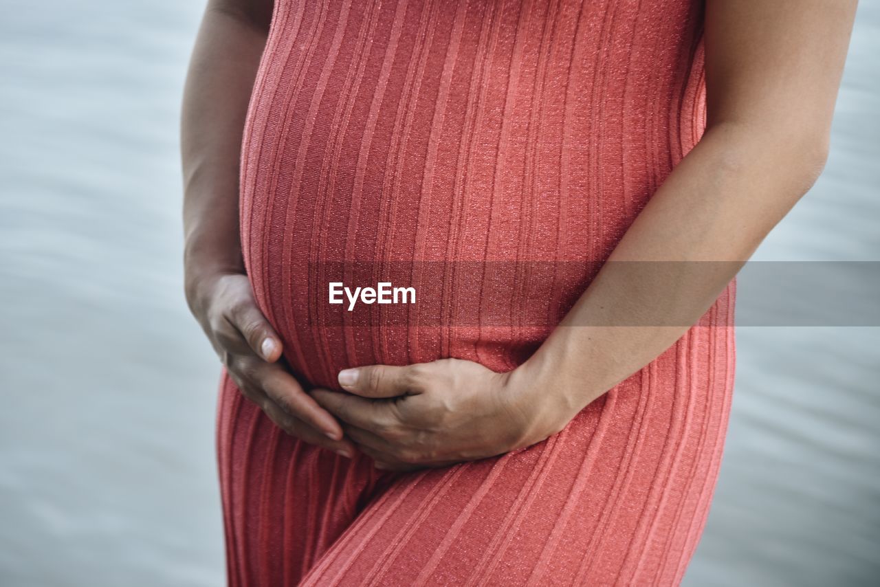 Midsection of pregnant woman standing by sea