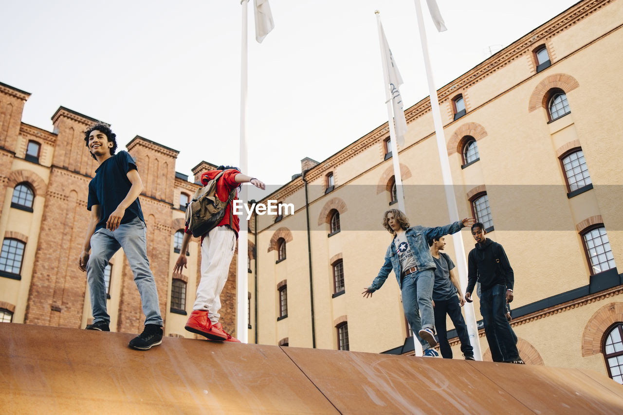 Low angle view of carefree playful friends walking on wall in city