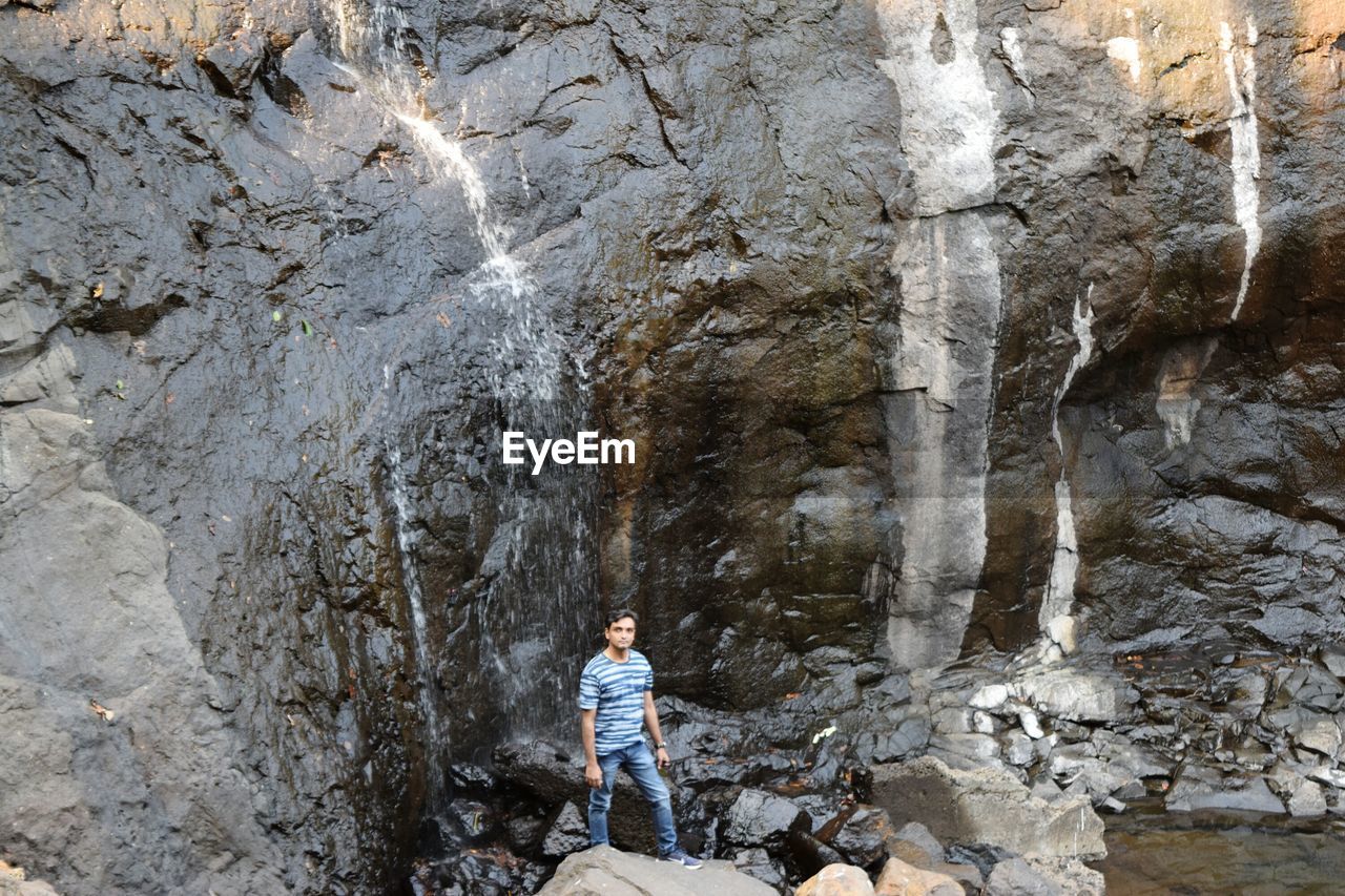 MAN STANDING ON ROCK BY CAVE