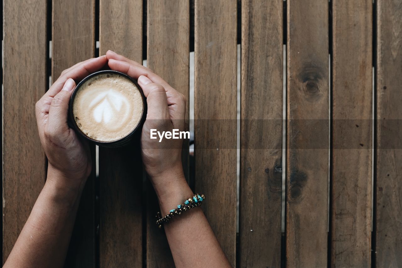 A close up shot of a woman holding a latte coffee cup on a wooden table