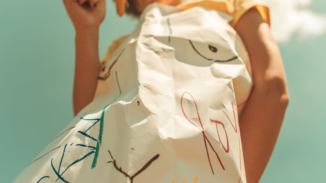 Low angle view of girl with paper standing against sky during sunny day