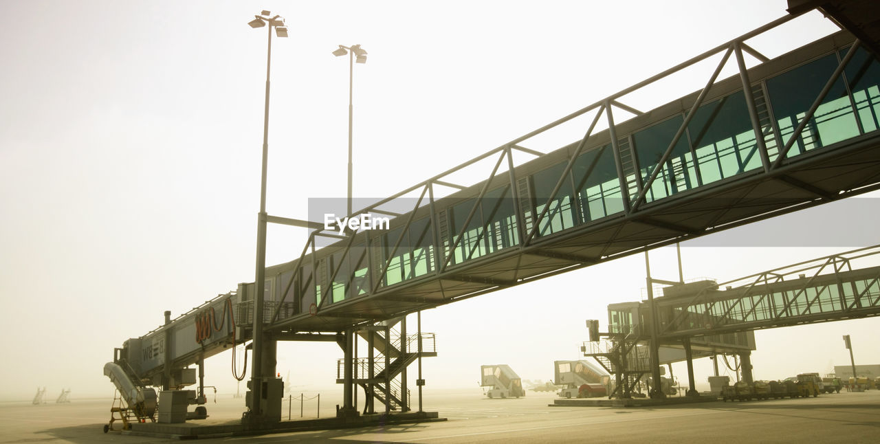 Passenger boarding bridges at airport runway against sky