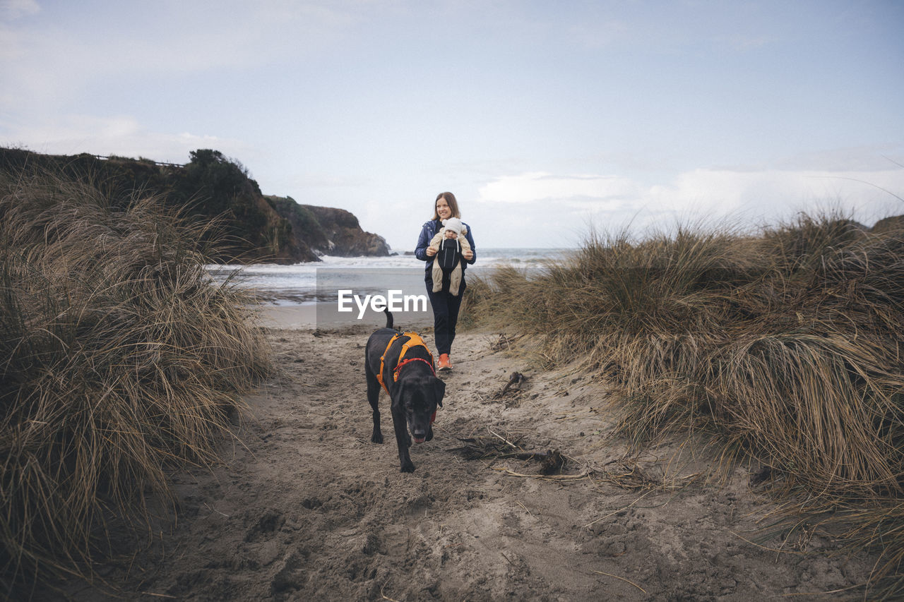 A woman with an infant is playing with a dog on the californian beach