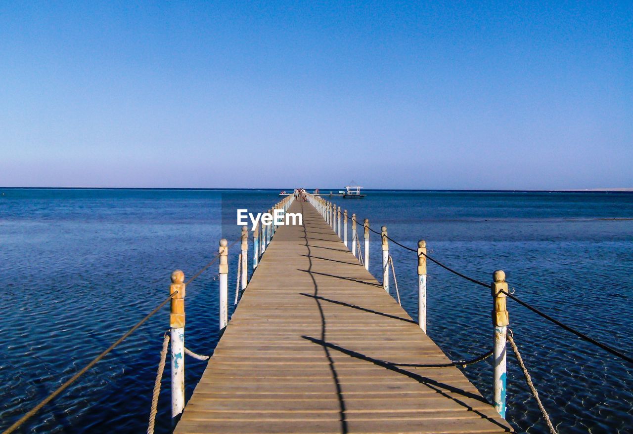 Pier over sea against clear blue sky