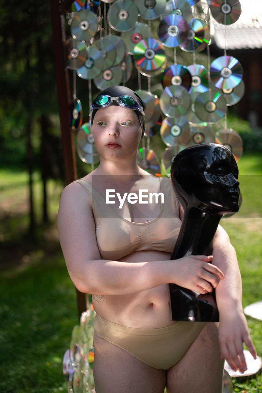 Portrait of a young woman in a pool cap against the background of a green garden and cd discs